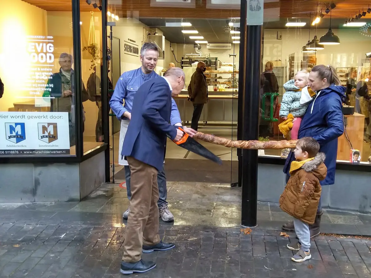 De bakker met zijn gezin. De wethouder opent de winkel met het doorzagen van een stokbrood.